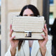 Person holding a textured handbag in front of their face with a blurred outdoor background