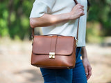 Person holding a brown leather bag outdoors